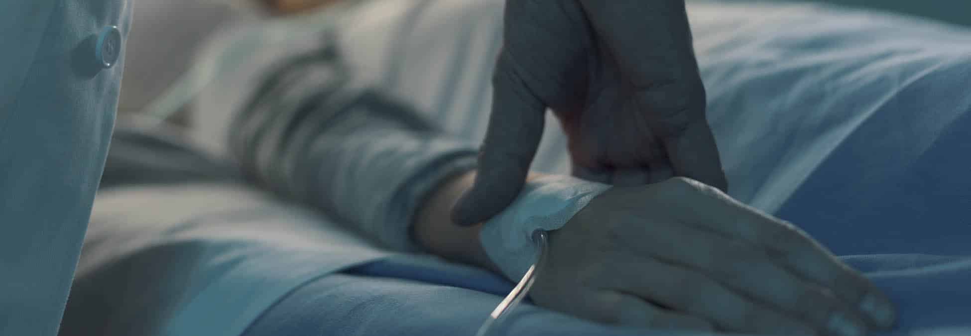 Doctor assisting a young patient at the hospital and taking pulse, she is lying on the bed and sleeping